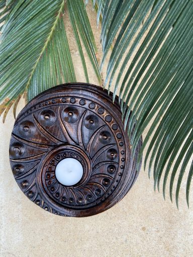 Soporte de vela en madera con diseño en espiral, junto a una hoja de palma.