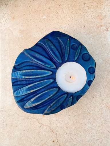 Vela blanca en un soporte azul con diseño de hojas.