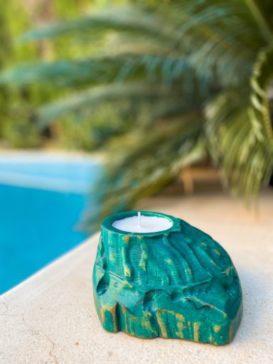 Portavelas verde en forma de roca, junto a una piscina y plantas al fondo.