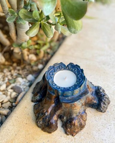 Soporte de vela en tronco de madera tallada, en tonos azules y marrones. 