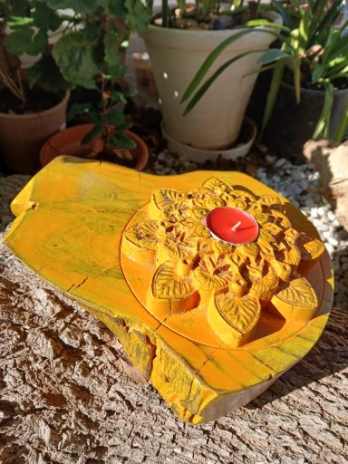 Portavelas amarillo con detalle floral y una vela roja en una base de piedra.