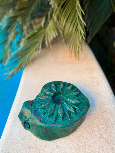 Objeto decorativo en forma de hoja con un diseño circular, de color verde oxidado.