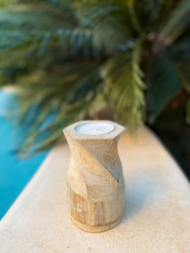 Soporte de vela en madera, en tonos beige, ubicada junto a una piscina y plantas verdes.